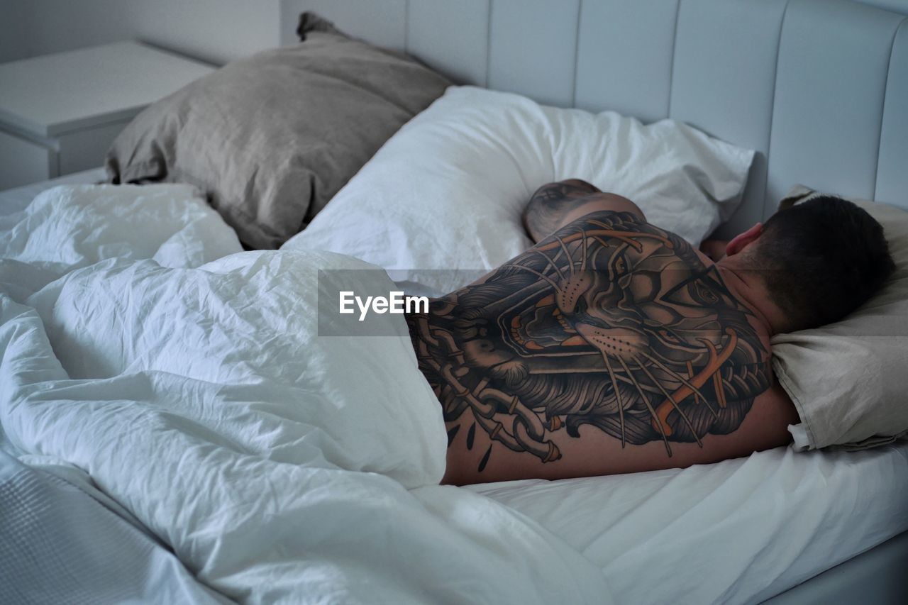 Rear view of man with tattoo sleeping on bed