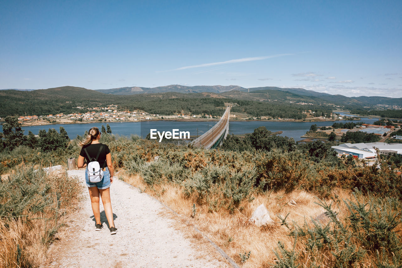 sky, water, nature, full length, sea, vacation, land, adult, rear view, mountain, holiday, leisure activity, coast, trip, travel, beach, women, plant, beauty in nature, scenics - nature, lifestyles, landscape, day, environment, walking, travel destinations, casual clothing, shore, two people, clear sky, men, sunlight, person, outdoors, sunny, tourism, activity, tranquility, young adult, transportation, togetherness, female, blue