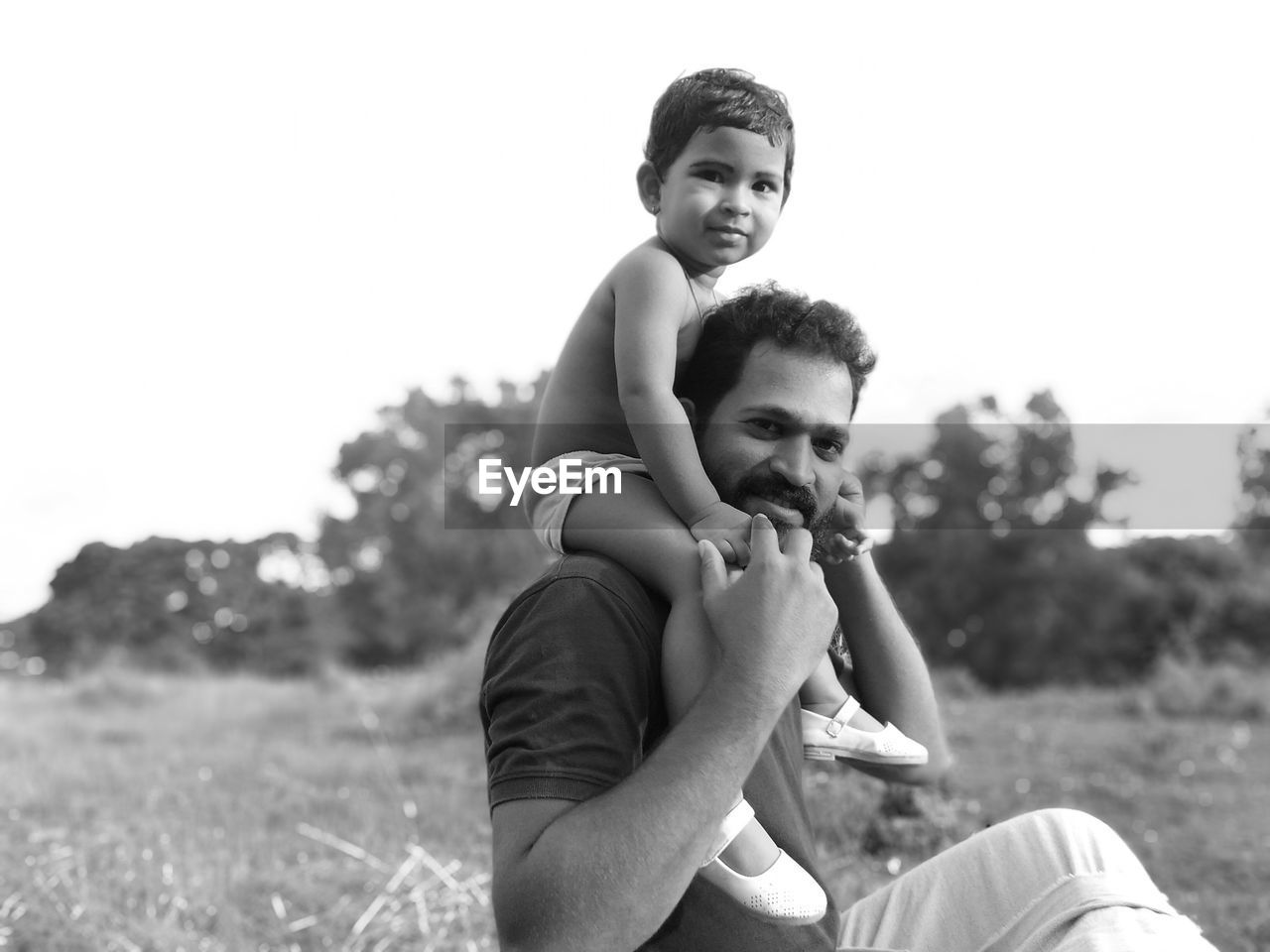 Portrait of baby girl with father sitting against sky
