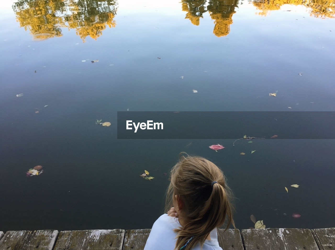 Rear view of girl sitting on pier over lake