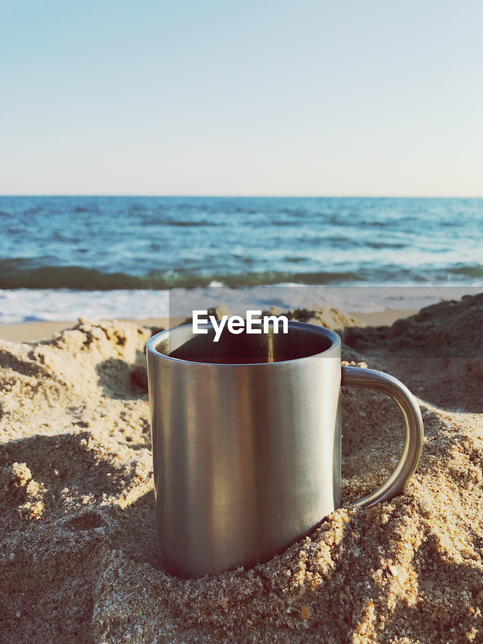 CLOSE-UP OF COFFEE CUP ON BEACH AGAINST SKY