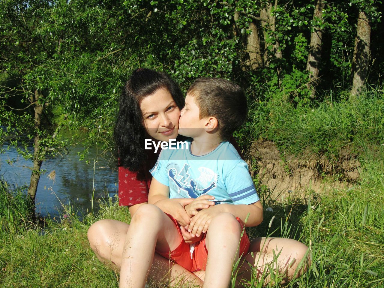 Boy kissing mother while sitting on grassy field