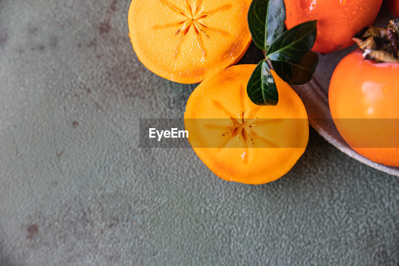 Whole and cut persimmon fruit with water drops and green leaves.