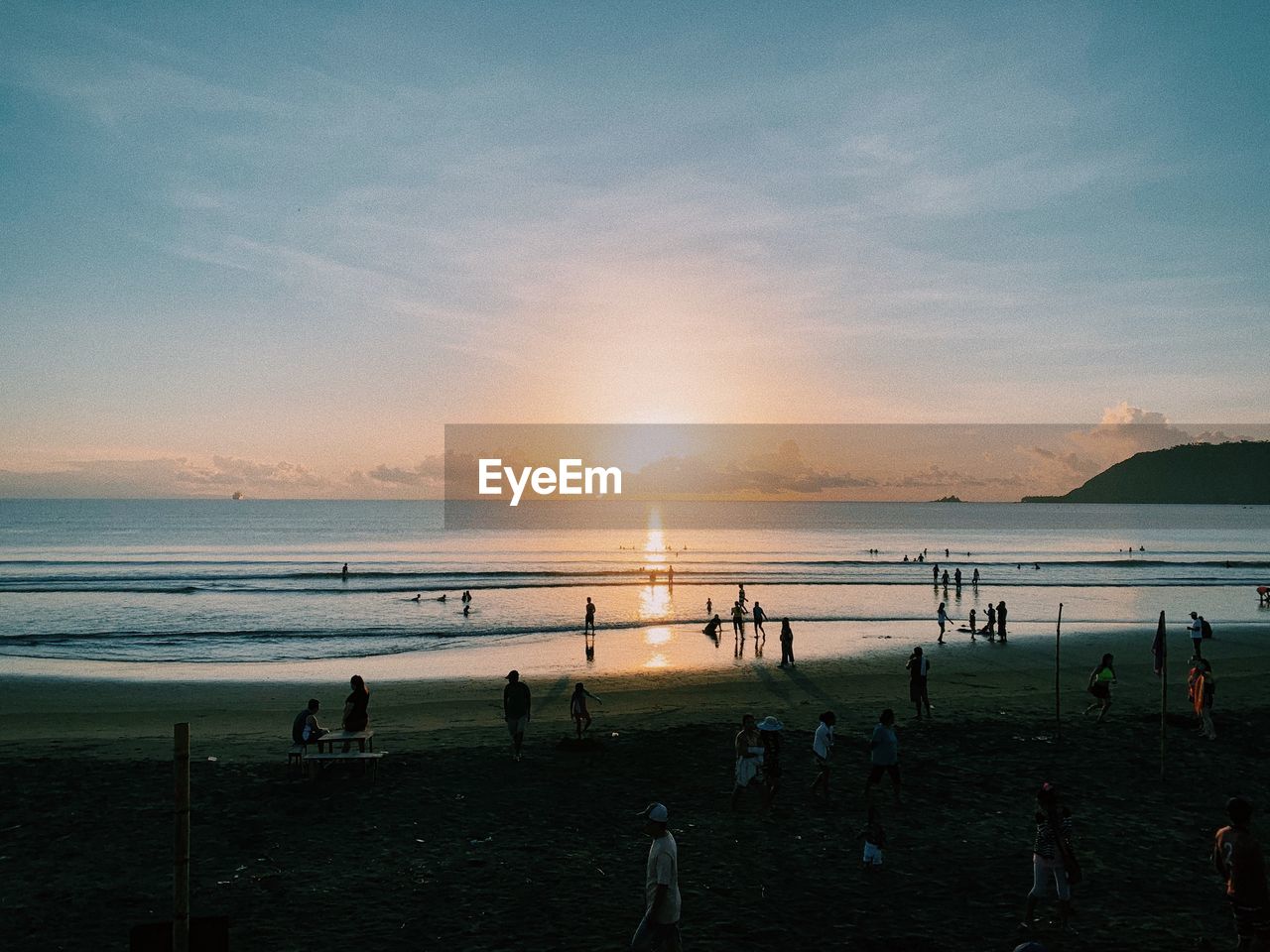 Group of people on beach against sky during sunset