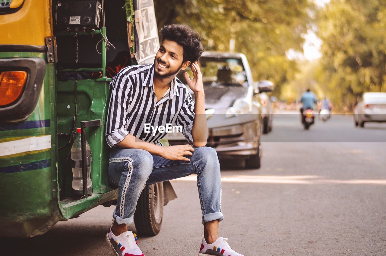 PORTRAIT OF YOUNG MAN SITTING ON ROAD