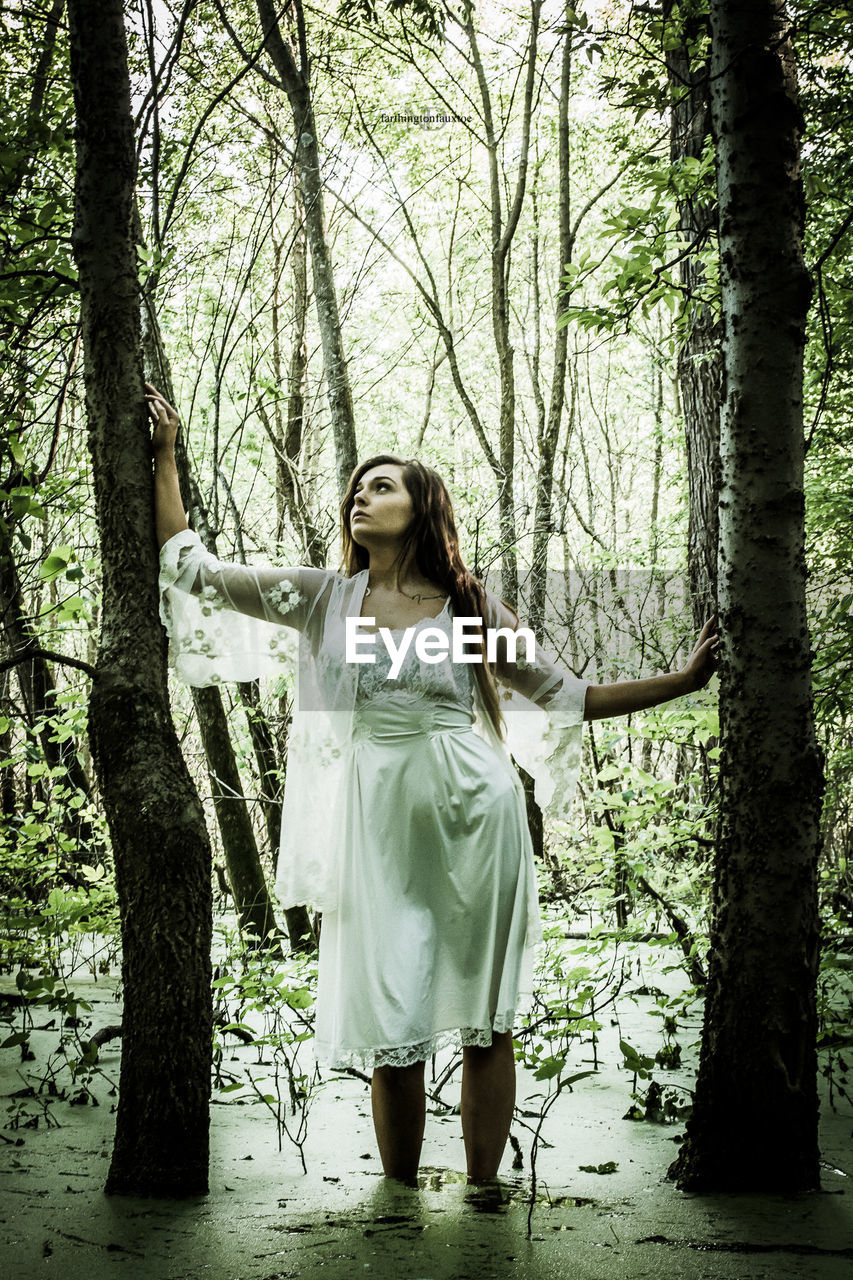 WOMAN STANDING BY TREE IN FOREST