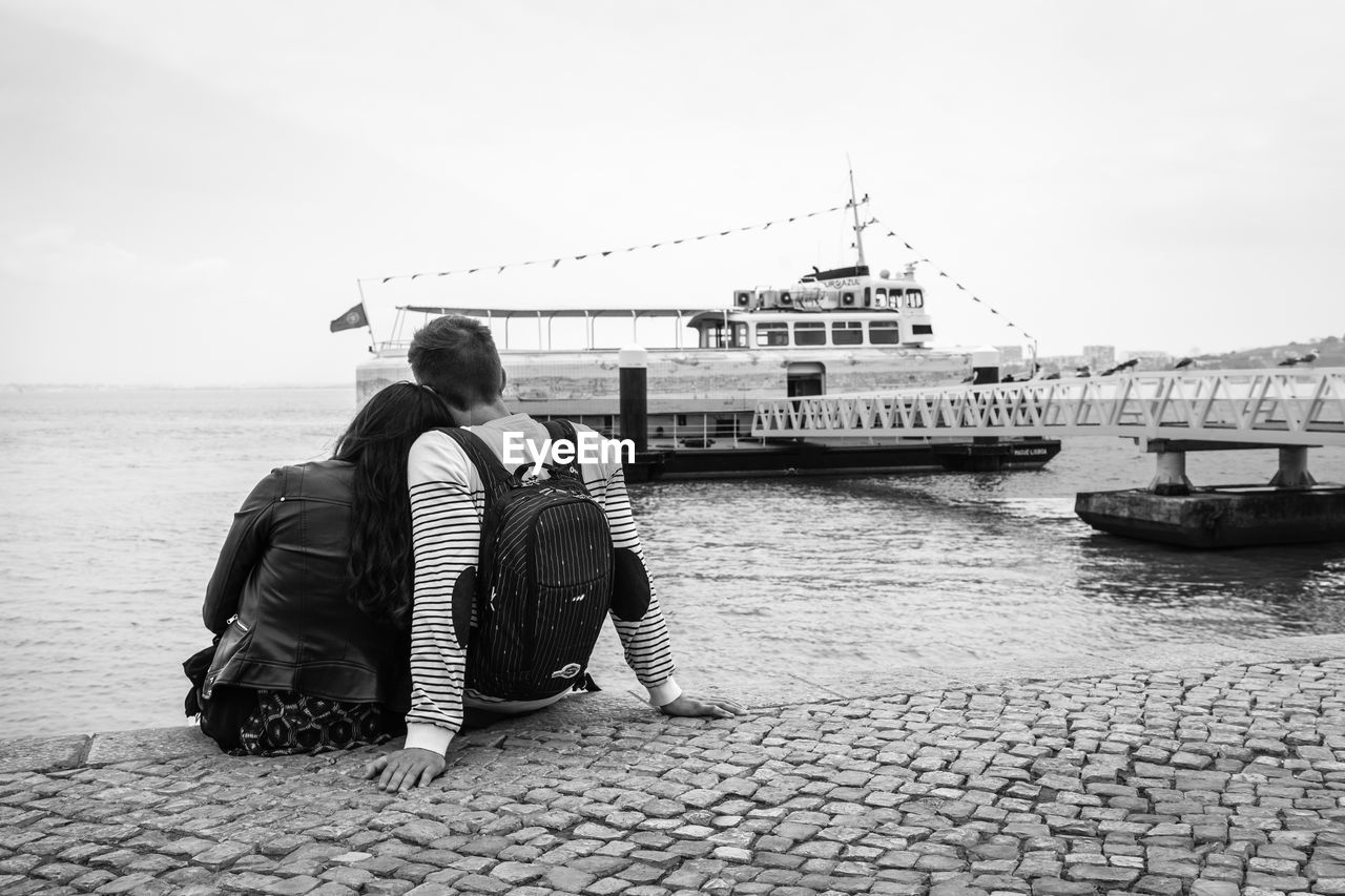 REAR VIEW OF MAN PLAYING GUITAR ON SHORE