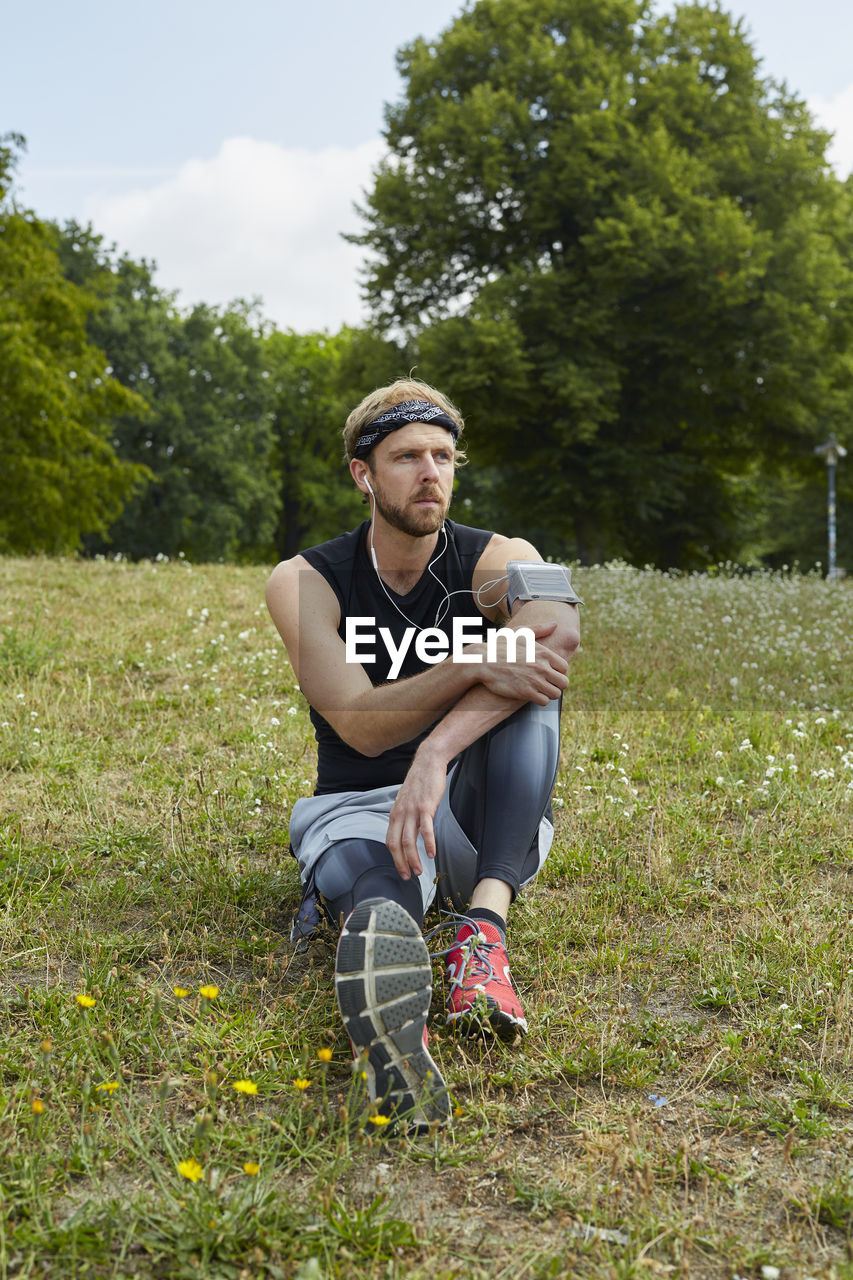 Man listening music while sitting on grassy land in park