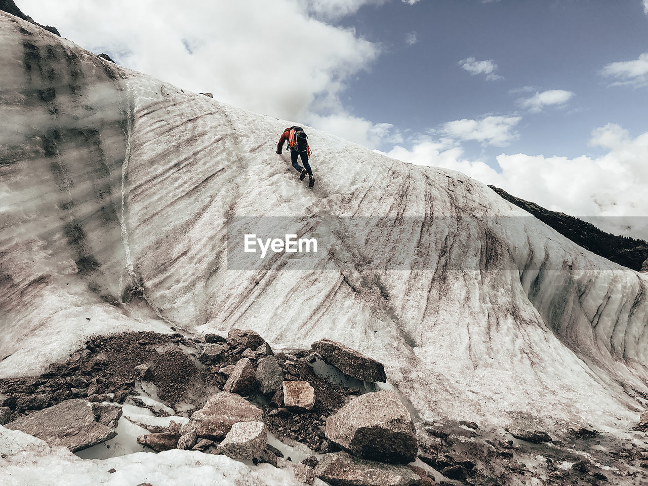 Mountaineer climbing up ice face next to running melt-water river