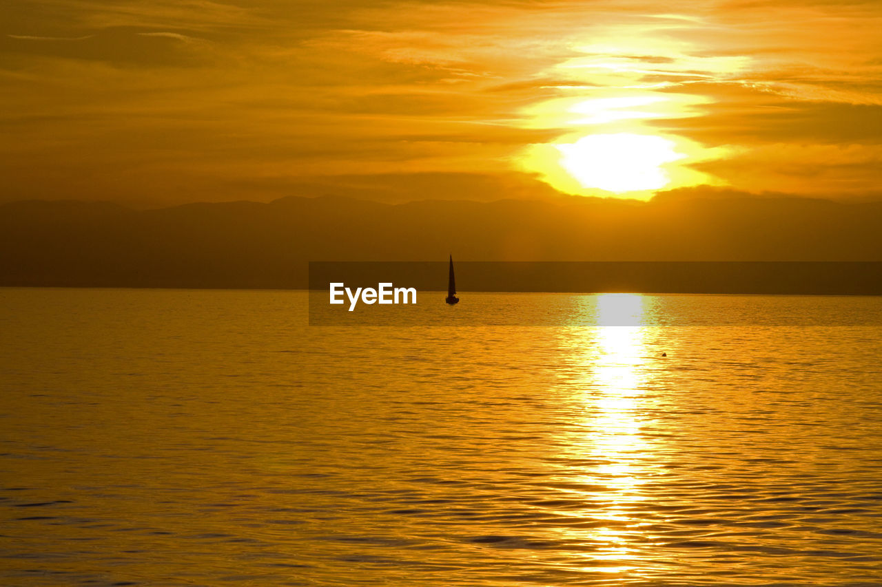 Scenic view of sail boat on lake geneva against orange sky at sunset