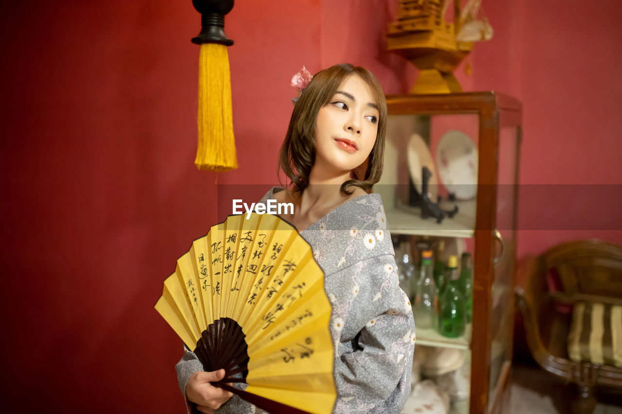 Close-up of woman holding hand fan at home