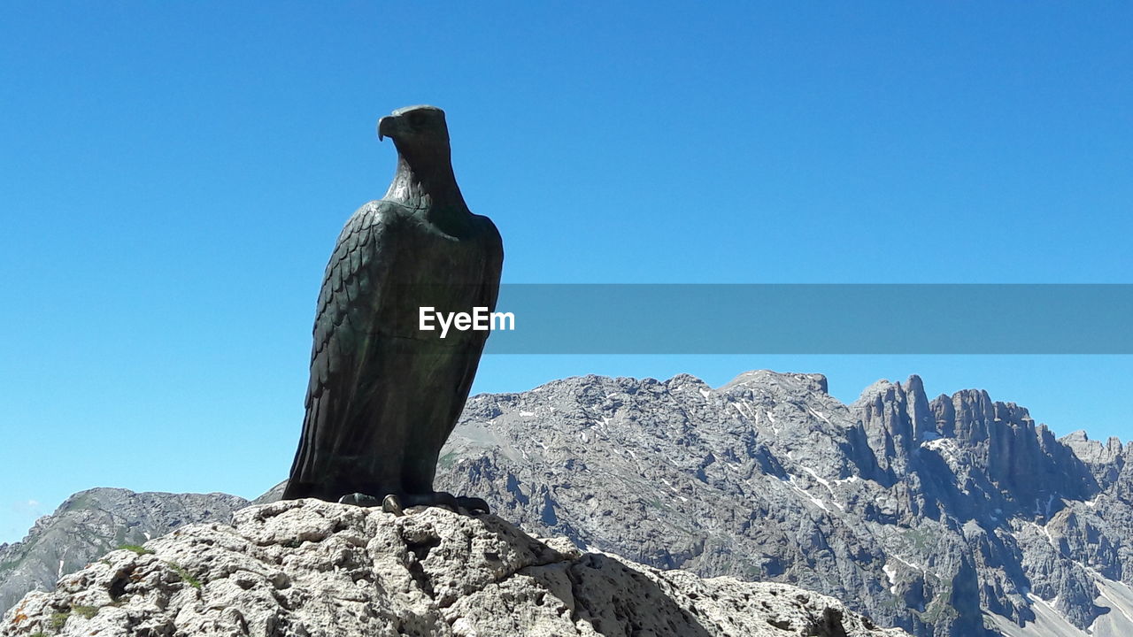 LOW ANGLE VIEW OF STATUE AGAINST ROCK FORMATION AGAINST CLEAR BLUE SKY