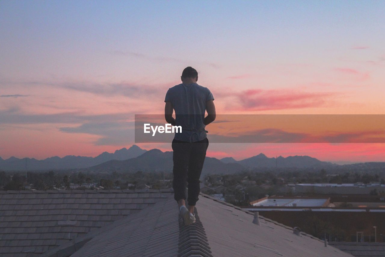 Rear view of man walking on rooftop against sky during sunset