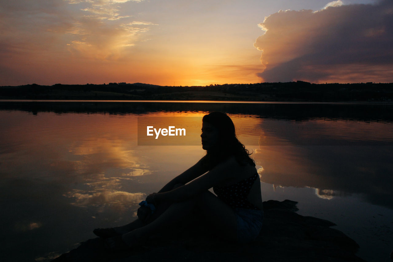 Silhouette woman standing by lake against sky during sunset