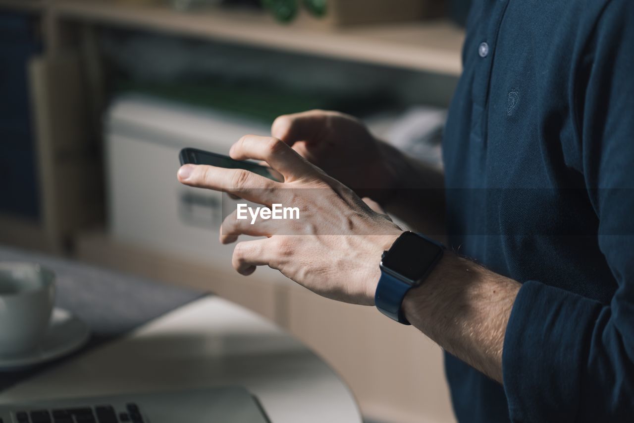 MIDSECTION OF MAN USING MOBILE PHONE IN KITCHEN