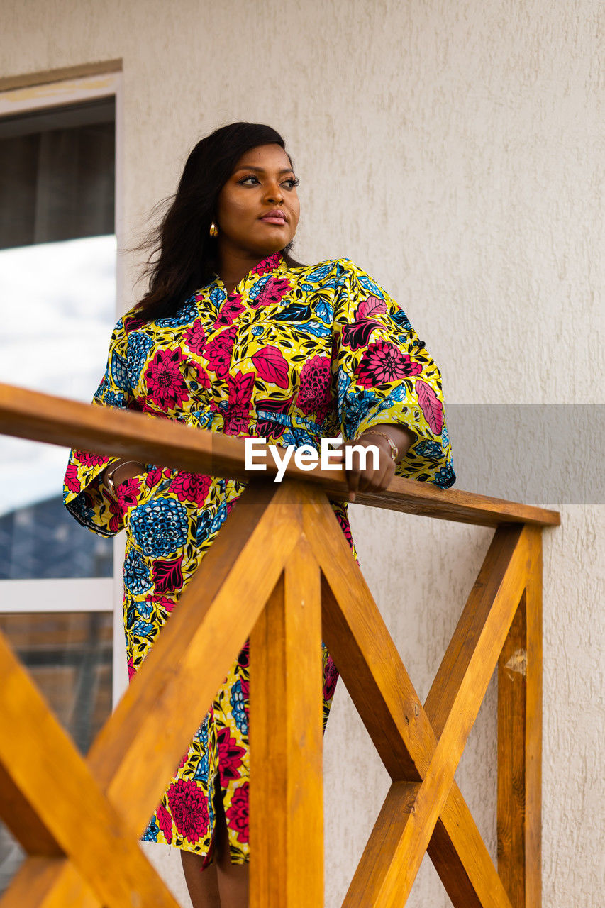 one person, yellow, women, adult, architecture, young adult, clothing, multi colored, wood, three quarter length, lifestyles, looking, portrait, standing, pattern, hairstyle, female, built structure, traditional clothing, building exterior, spring, fashion, smiling, sitting, building, leisure activity, front view, looking away, outdoors, relaxation, happiness, day