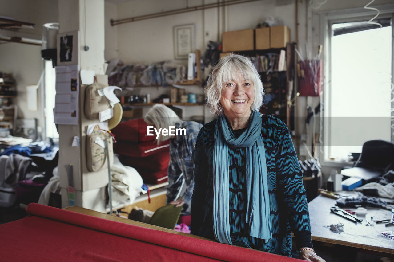 Portrait of smiling senior female standing at workbench in workshop