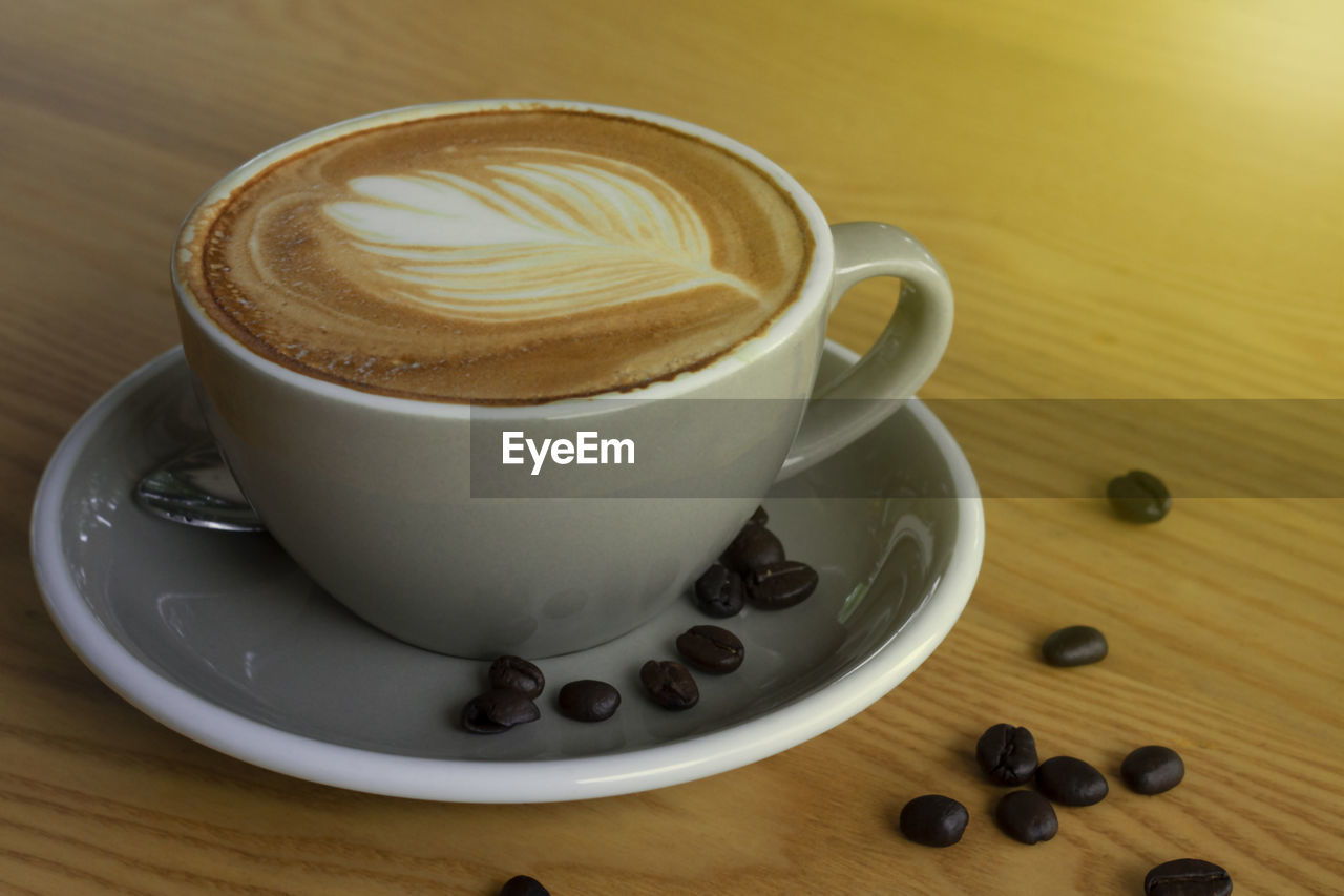 Latte art heart coffee and roasted coffee beans on wooden table