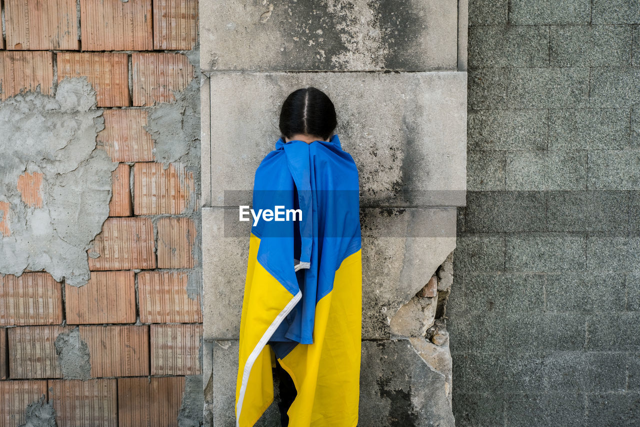 Girl wrapped in ukrainian flag against wall