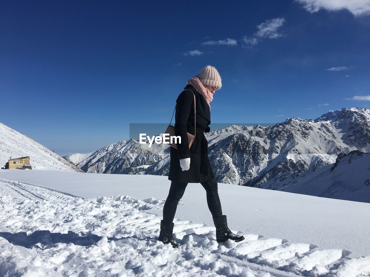 Side view of young woman walking on snowcapped mountain against blue sky