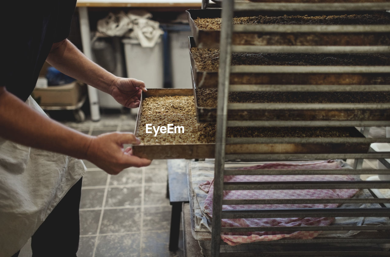 Midsection of baker keeping baked breads in tray on cooling rack at bakery