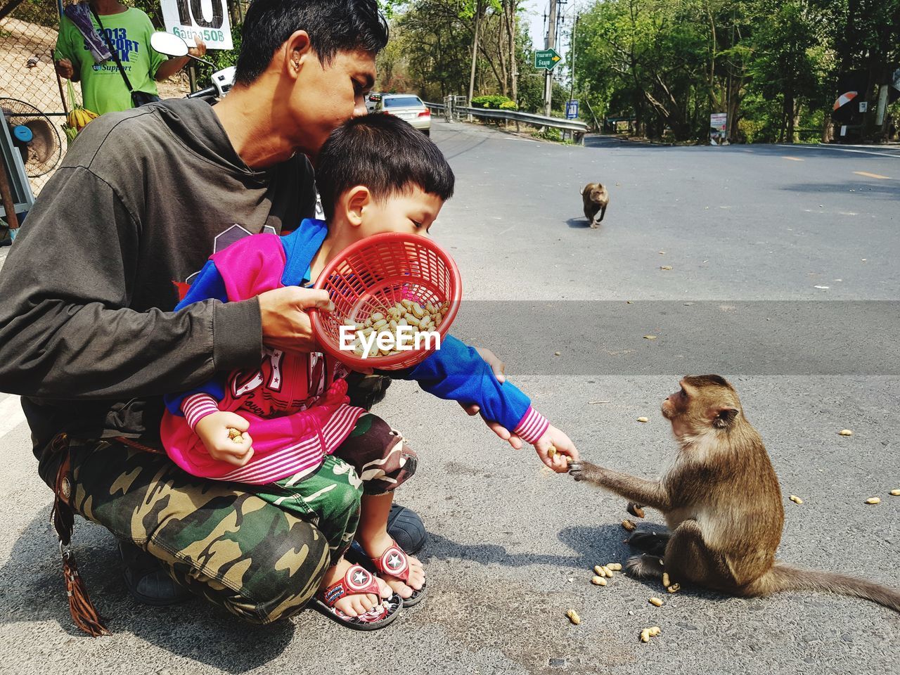 Father and son feeding monkey while crouching on road