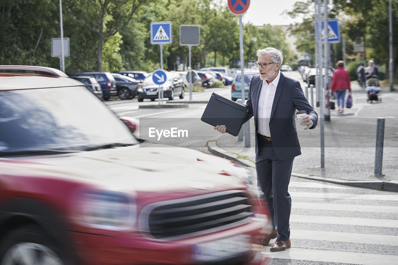 Shocked senior male professional crossing by speeding car