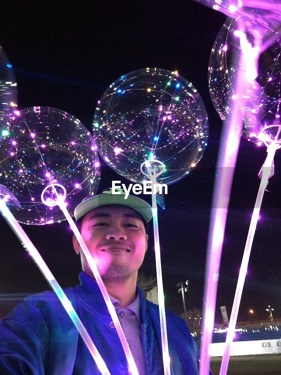 Portrait of smiling man holding illuminated balloons at night