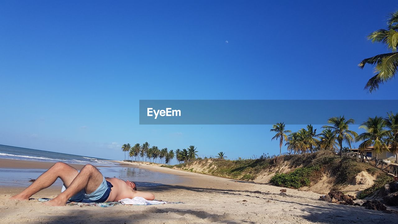 WOMAN RELAXING ON BEACH AGAINST BLUE SKY