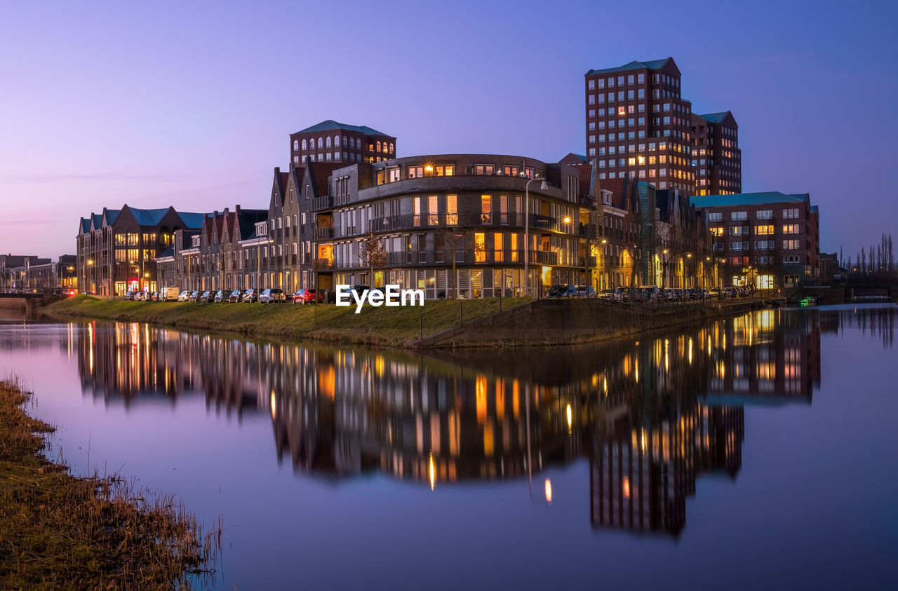 ILLUMINATED BUILDINGS BY LAKE AGAINST SKY AT DUSK