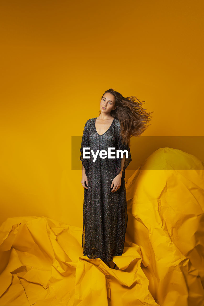 Young woman standing against yellow background