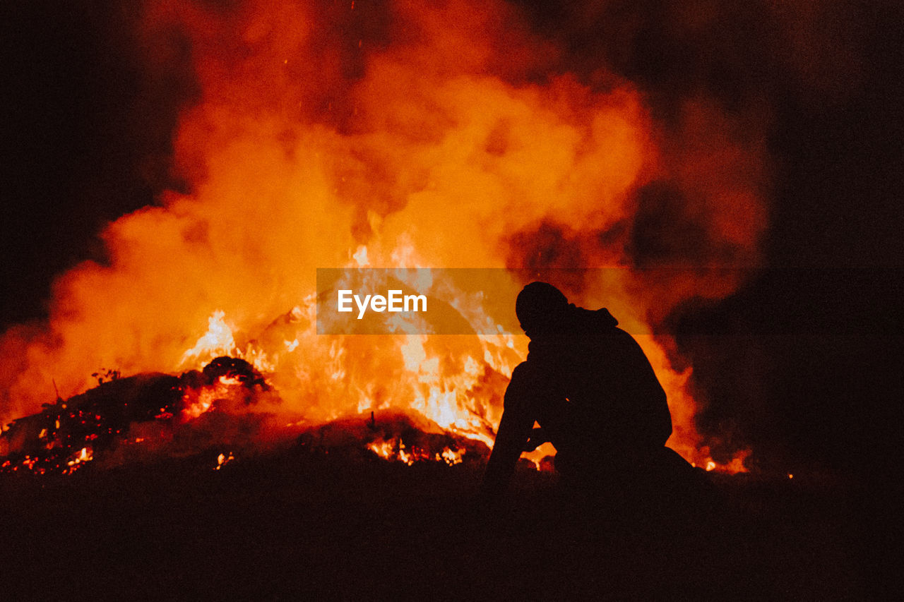 Silhouette man sitting by bonfire at night