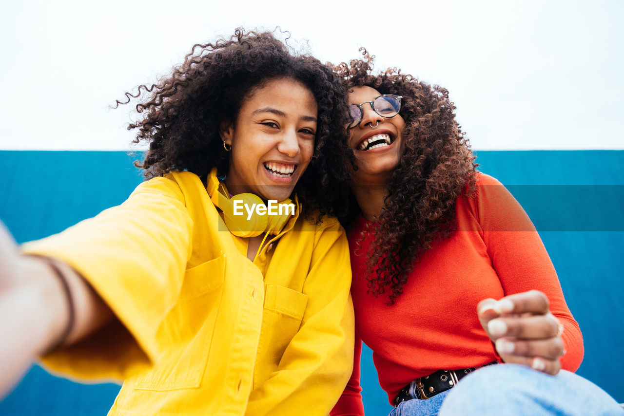 Smiling female friends sitting against wall