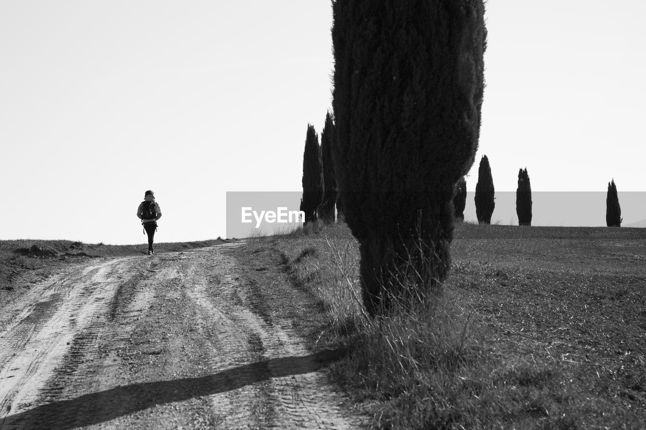 REAR VIEW OF MAN WALKING ON FIELD AGAINST CLEAR SKY