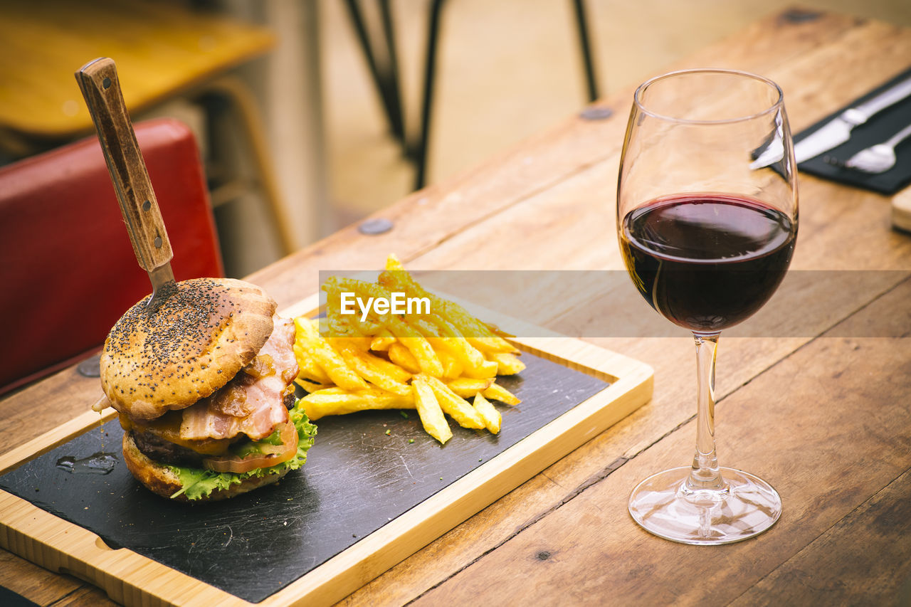 High angle view of french fries and burger by red wine served on wooden table