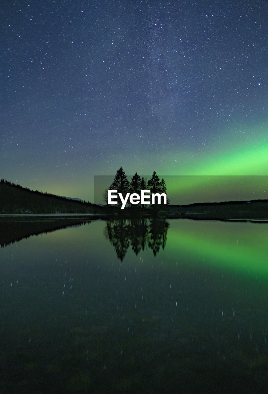 Starfield with aurora borealis reflections in a still lake with small island in the center