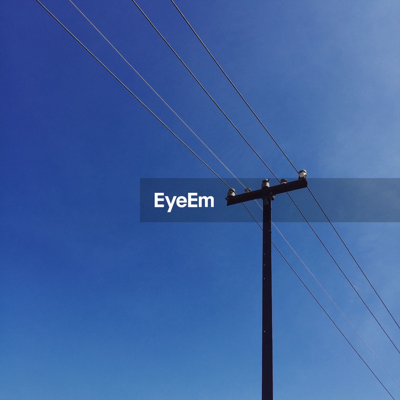 Low angle view of electricity pylon against clear blue sky