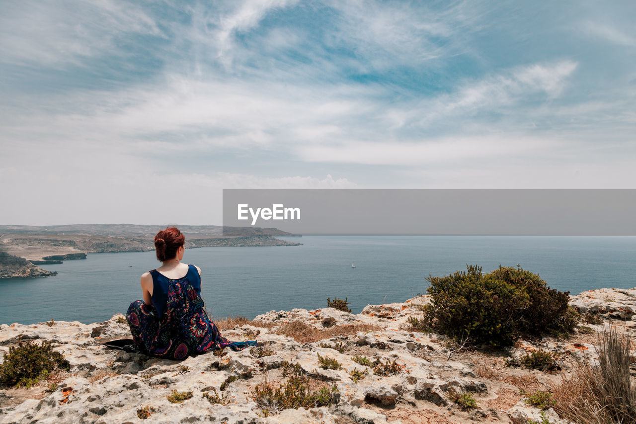 Rear view of woman sitting on cliff against sea