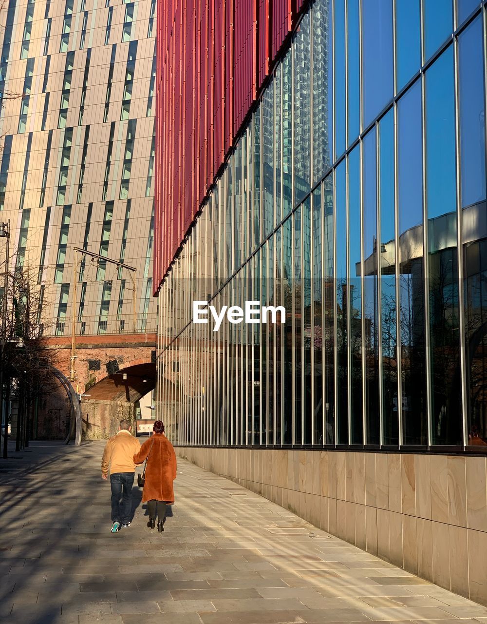 REAR VIEW OF PEOPLE WALKING ON STREET AGAINST BUILDINGS