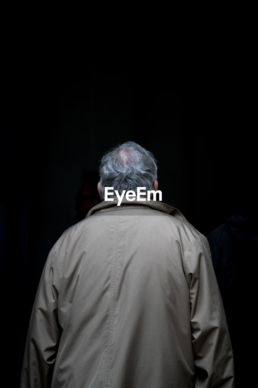 REAR VIEW OF MAN WEARING HAT AGAINST DARK BACKGROUND