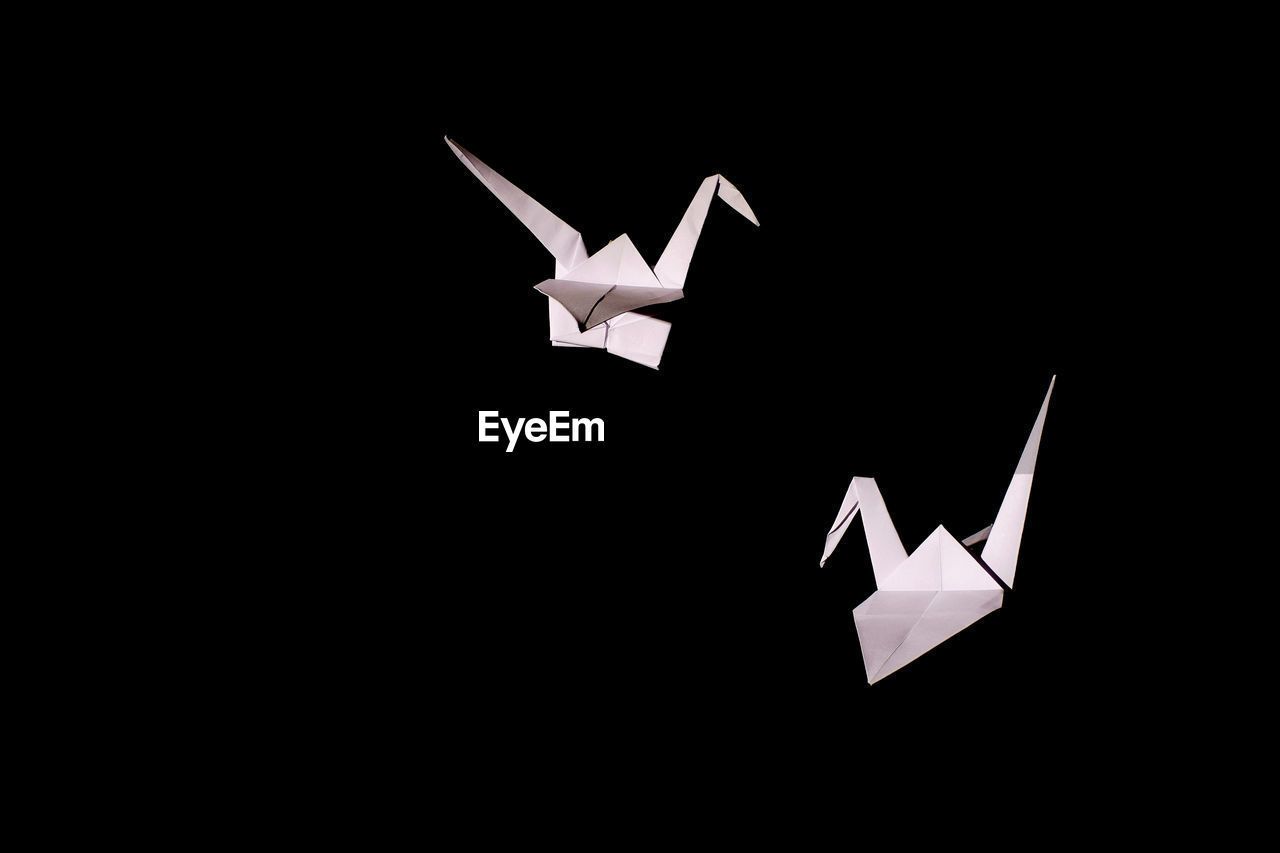 Origami cranes in mid-air against black background