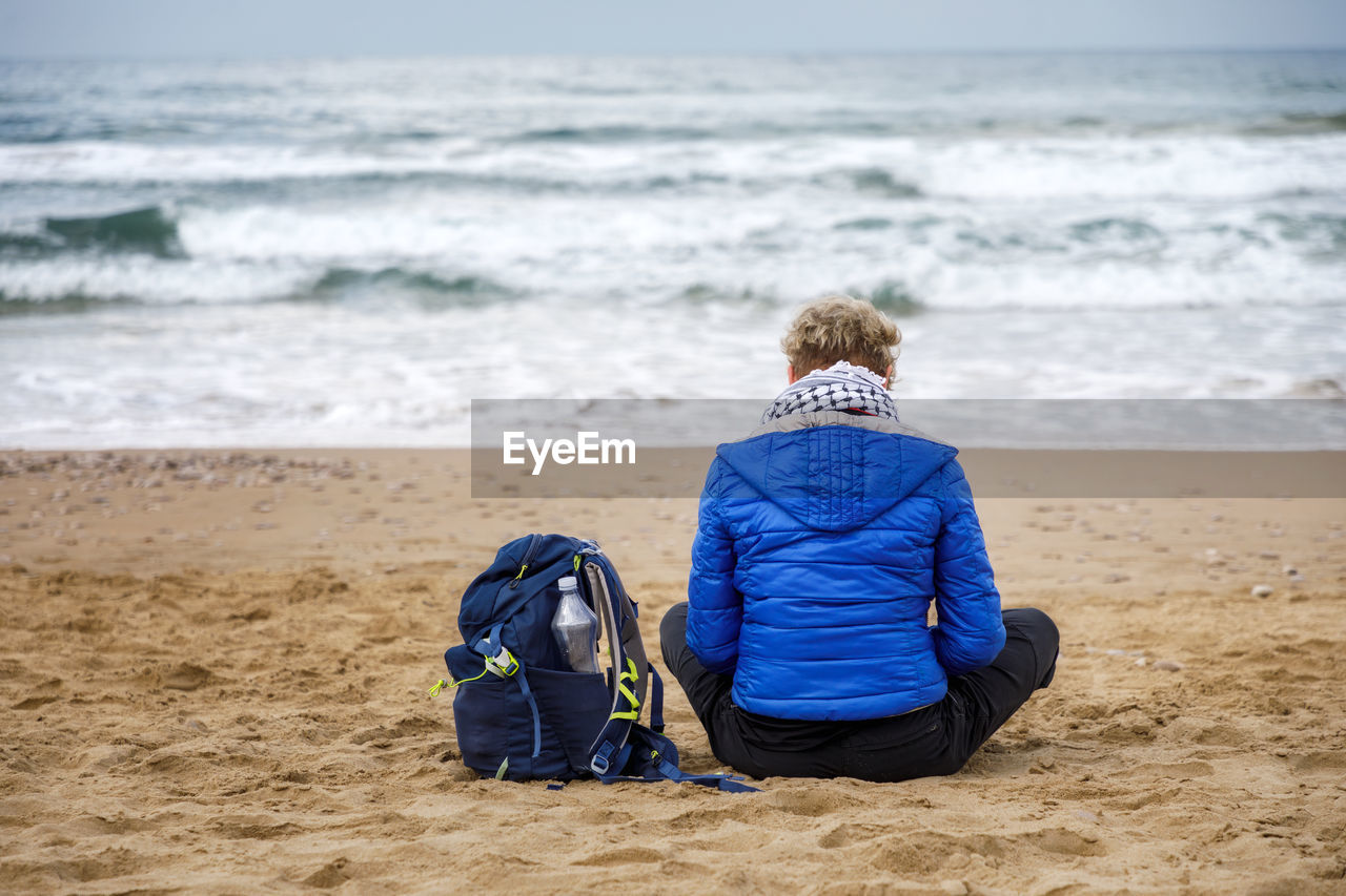 Woman sitting on the beach practicing meditation observing the horizon of the stormy sea. 