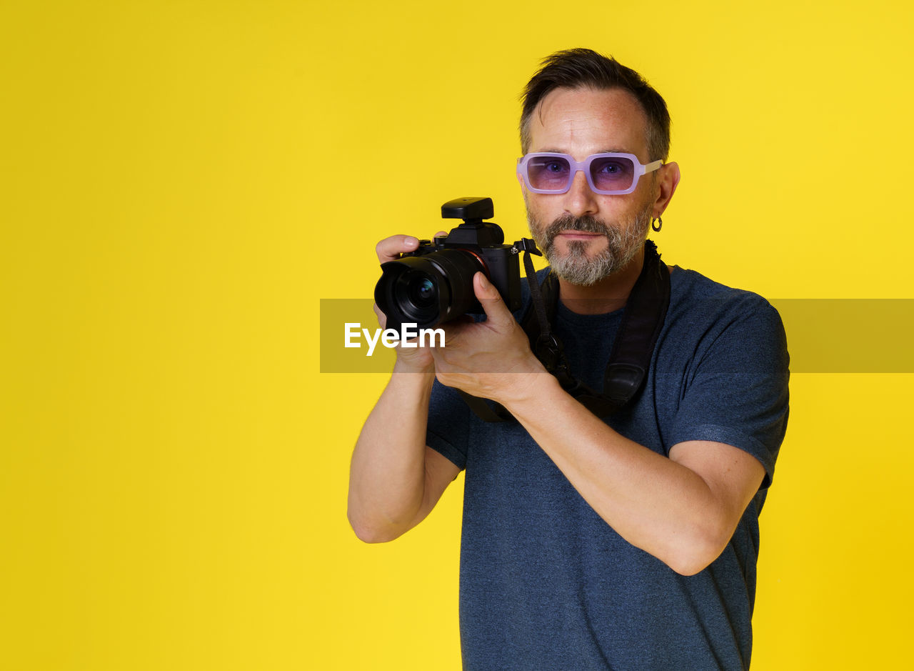 man photographing with camera against yellow background