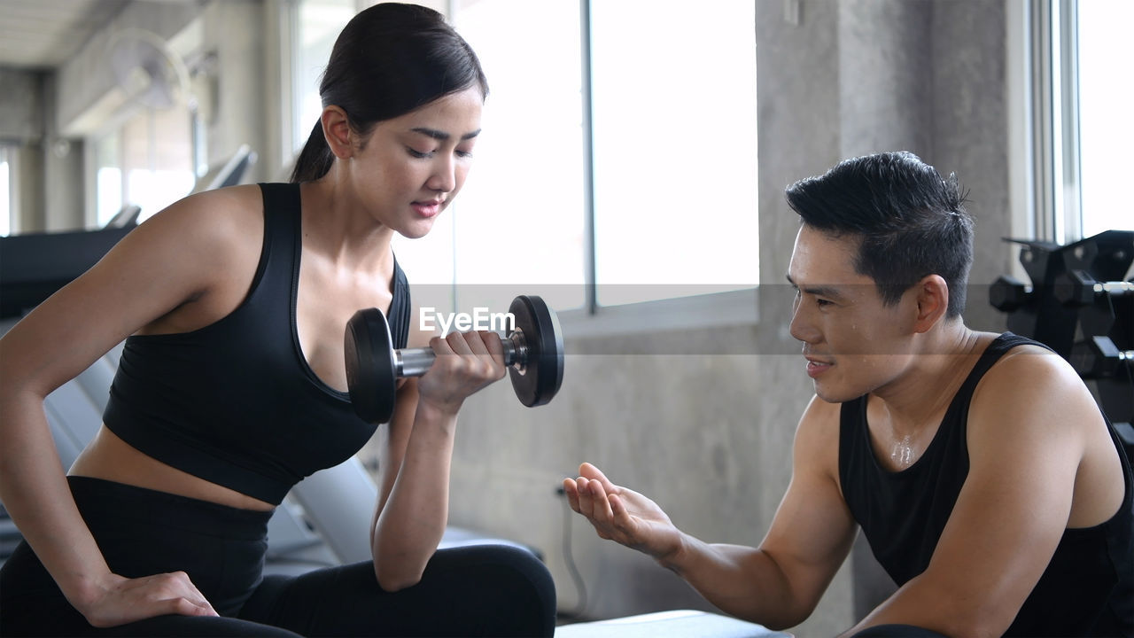 Instructor assisting woman in exercising at gym