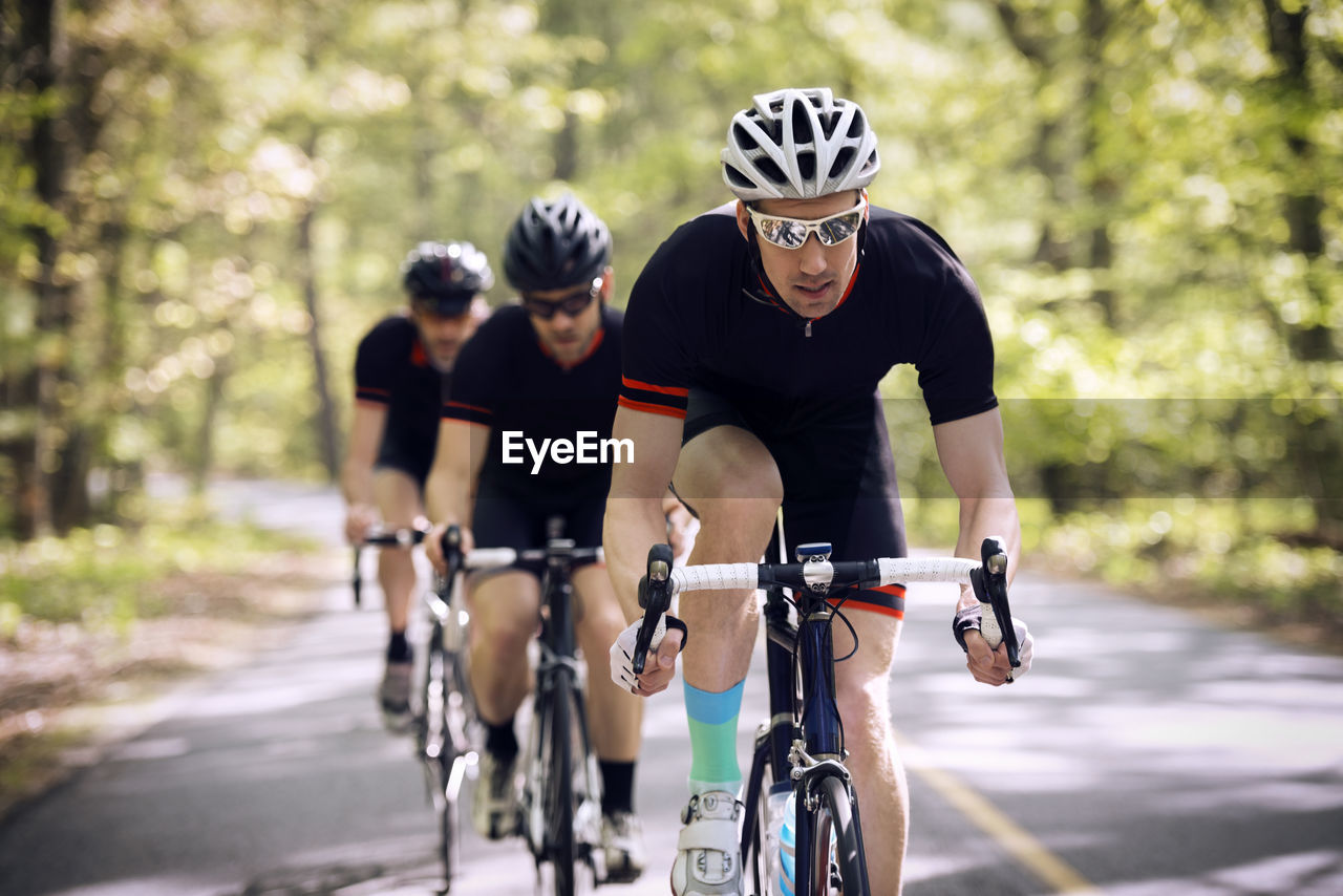 Confident male cyclist riding bicycle with friends on country road