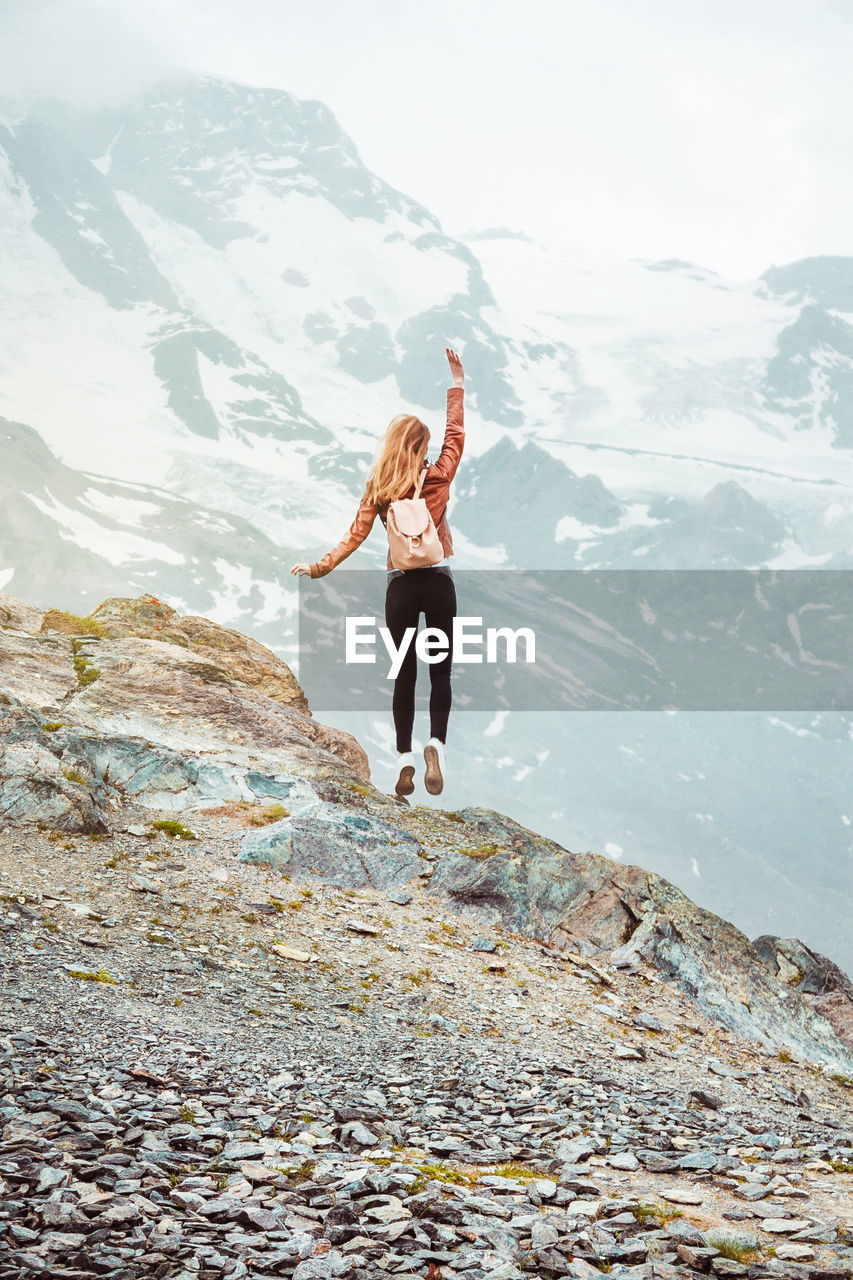 Jumping woman with backpack on mountain background. top of gornergrat, zermatt, swiss. alps hiking