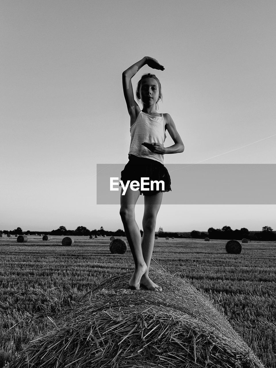 Full length portrait of girl standing on hay bale at field