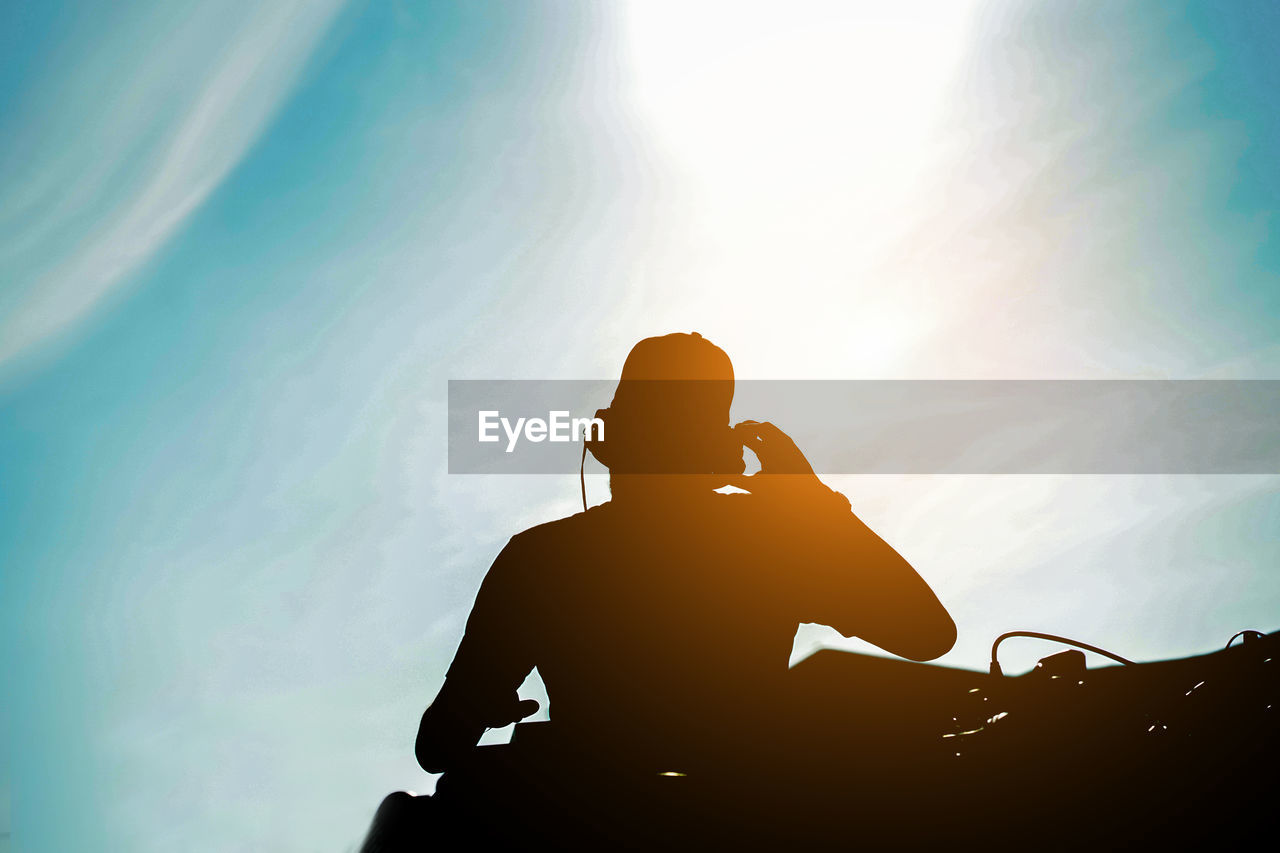 Low angle view of silhouette man listening music against sky