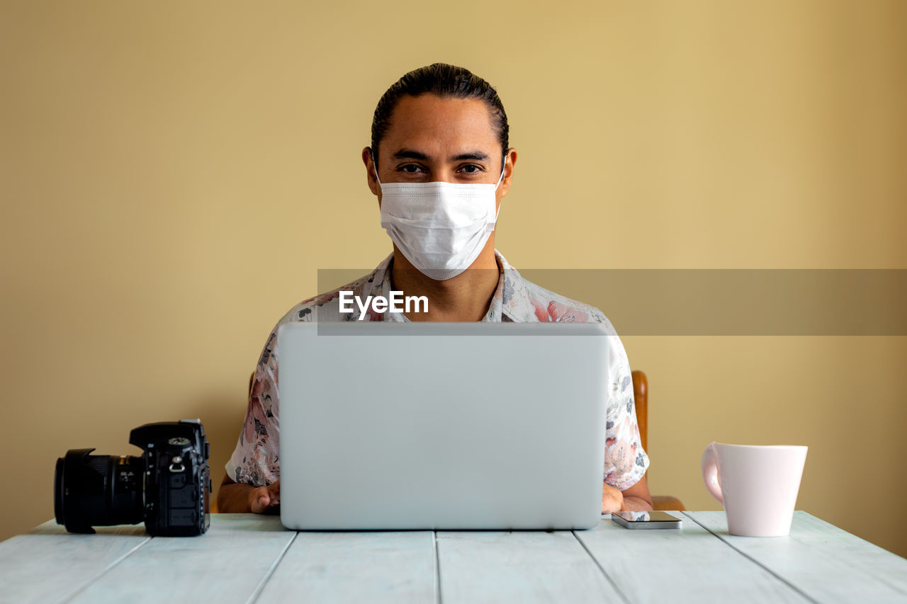 Portrait of man wearing mask while using laptop