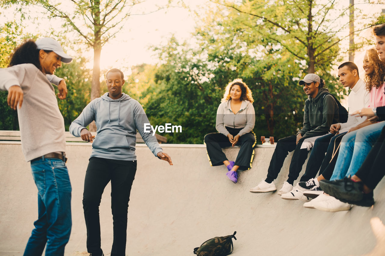 Friends looking at men dancing in skateboard park